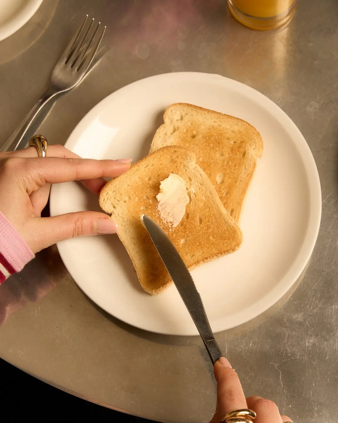 Two hands buttering toast on a steel table