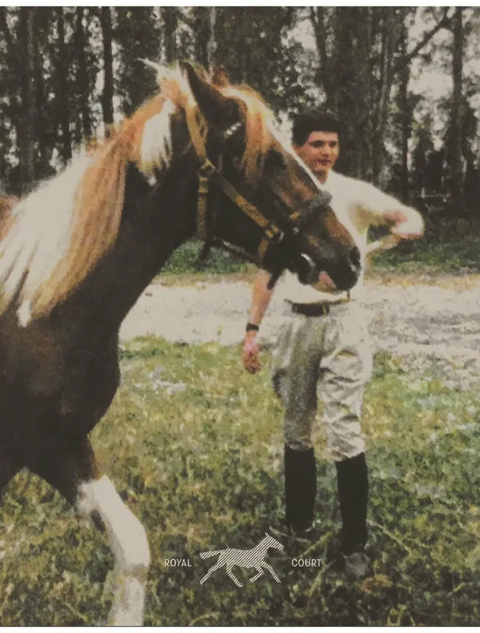 An archival photograph of a young man leading a pinto horse across grass