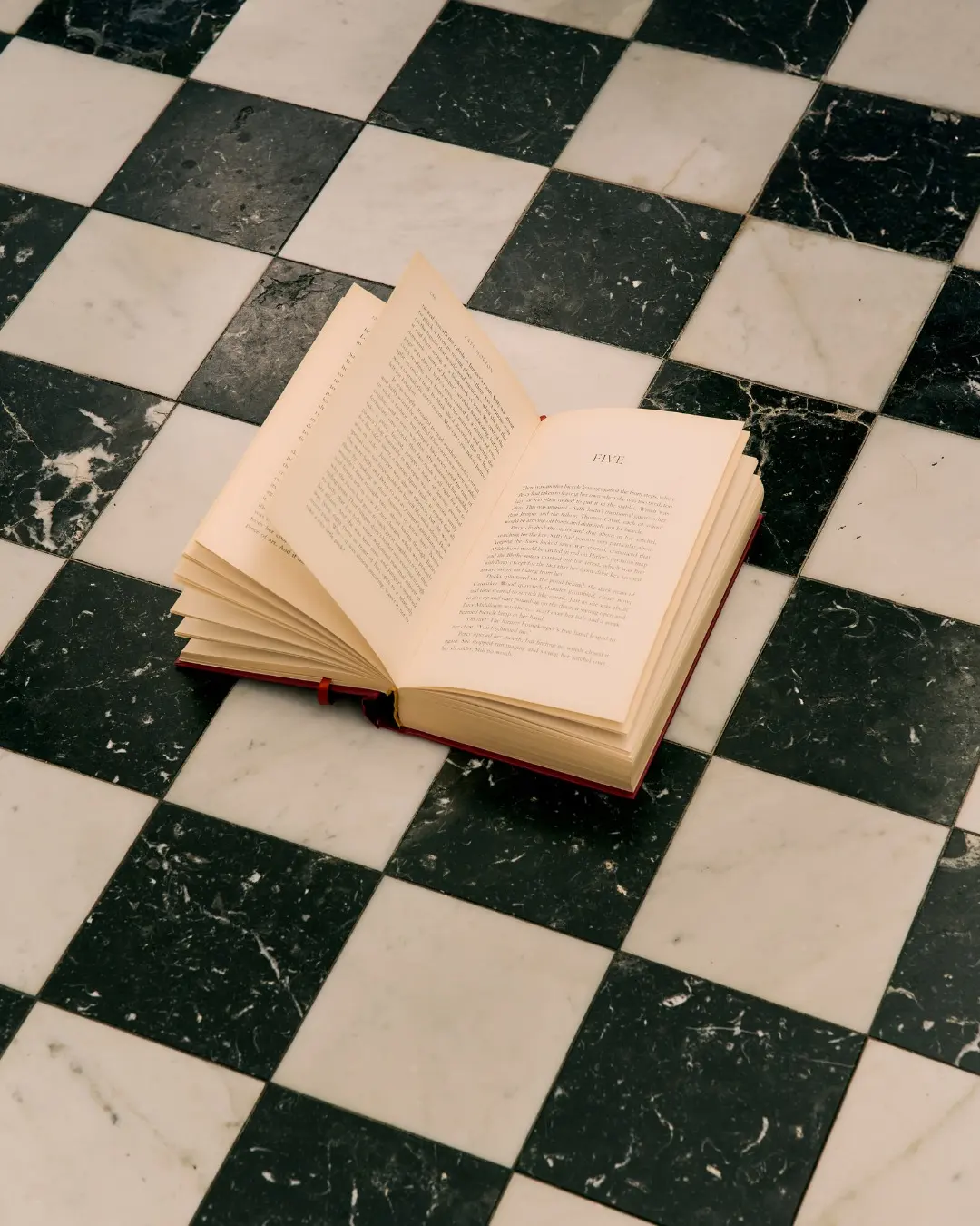 An open book left face down on a checkerboard marble floor