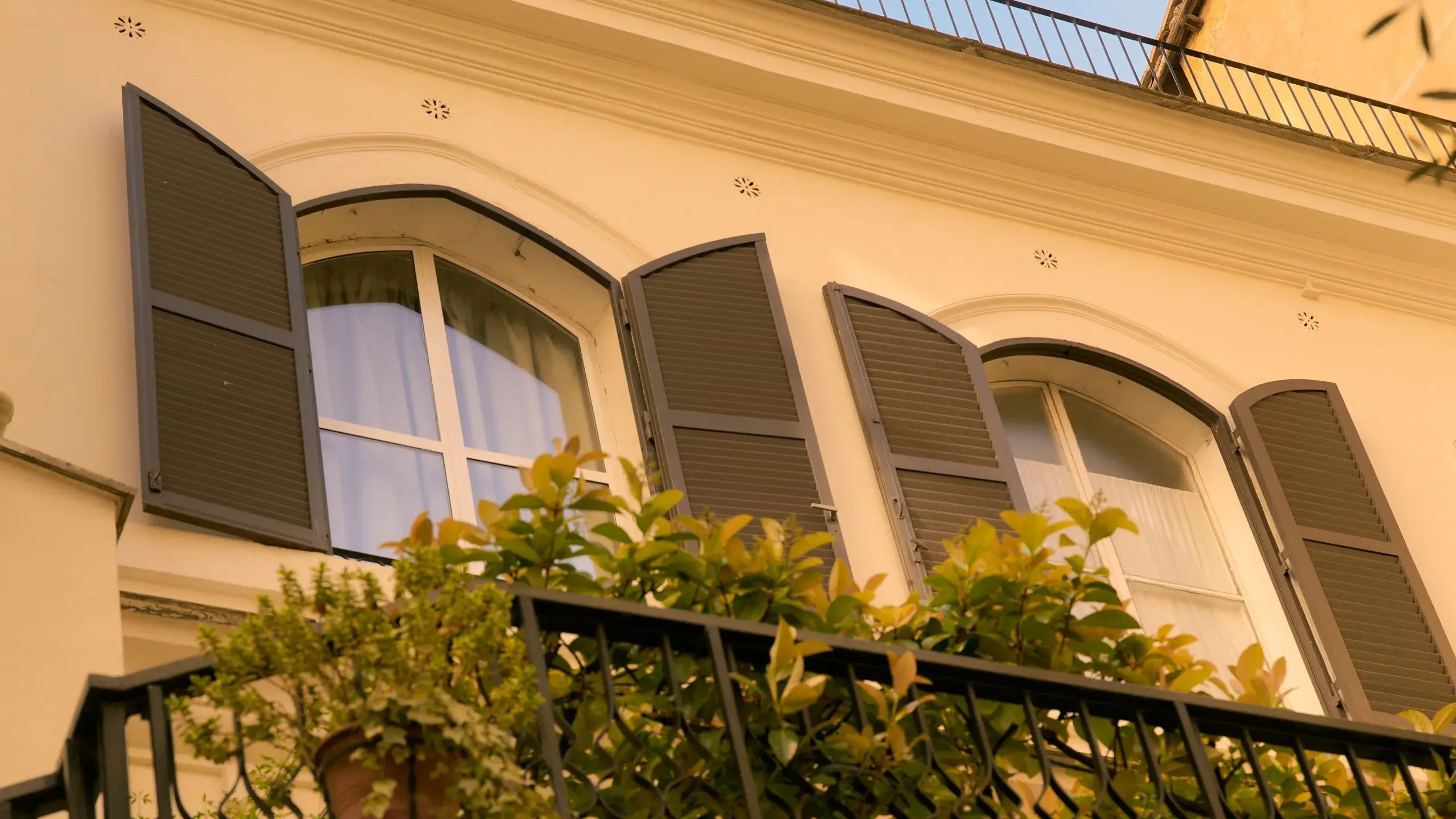 Two arched shuttered windows above a balcony of plants on the Royal Court facade
