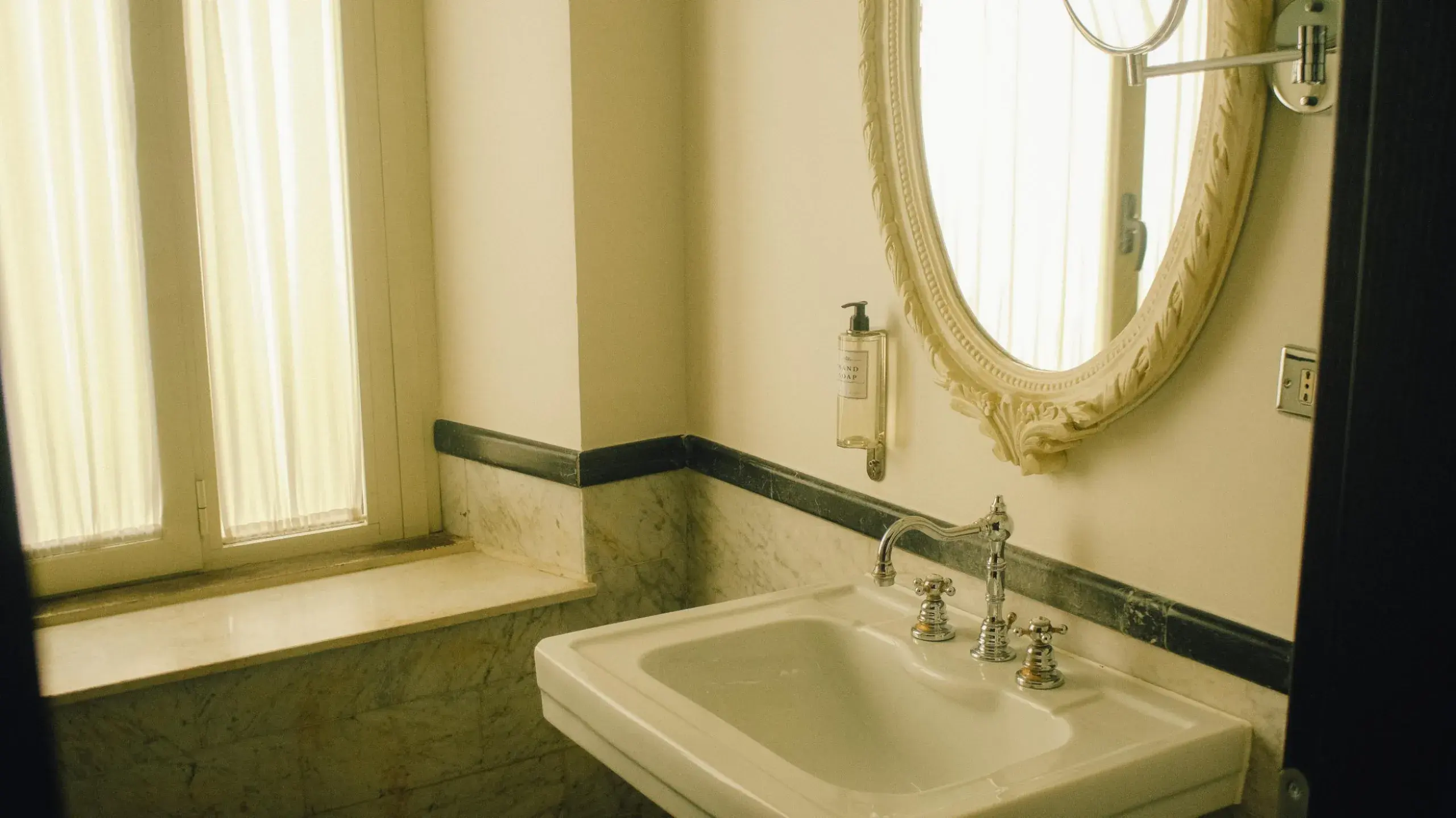 A bathroom basin below an oval mirror, green marble at the sill