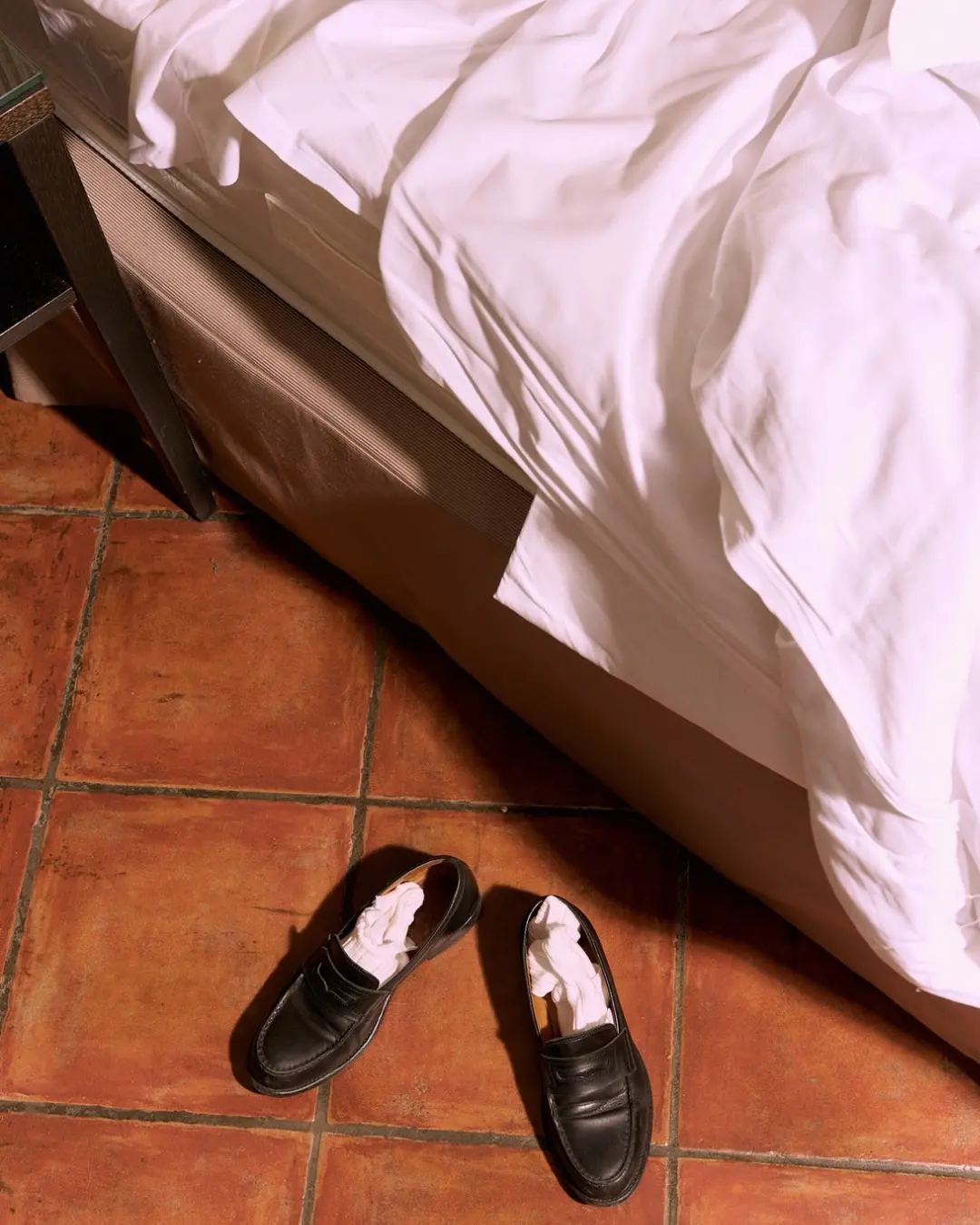A pair of loafers kicked off on a terracotta floor beside the bed